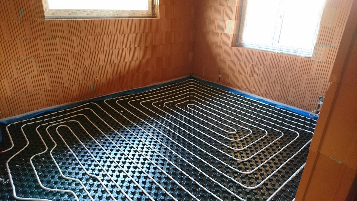 Podlahové kúrenie rozložené na systémovej doske v izbe tehlovej hrubej stavby